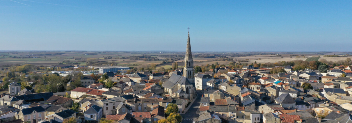 Vue aérienne de Mirebeau (Vienne), avec son église au centre du bourg, entourée de maisons en pierre et toitures en tuiles, dans un paysage rural et vallonné.