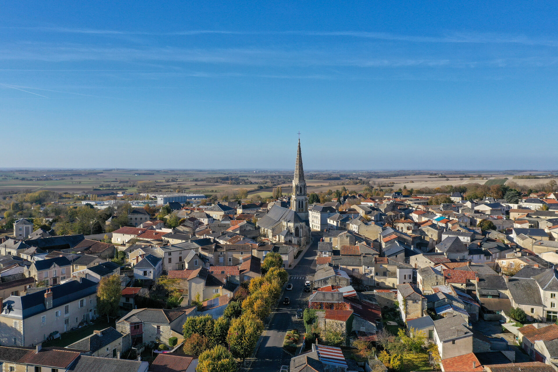 Vue aérienne de Mirebeau (Vienne), avec son église au centre du bourg, entourée de maisons en pierre et toitures en tuiles, dans un paysage rural et vallonné.